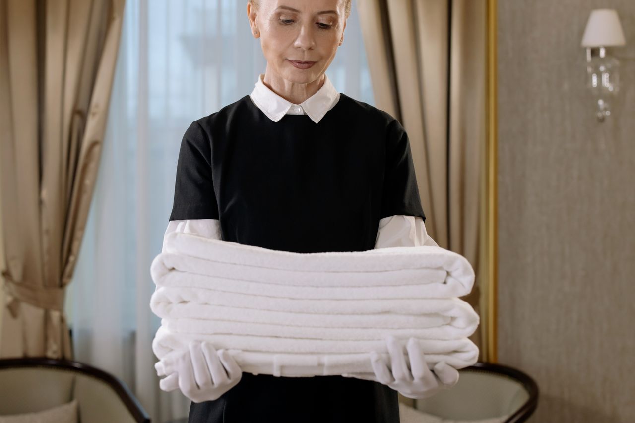 services-03 Professional housekeeper holding a stack of fresh towels in a luxurious hotel room, showcasing elegance and service.